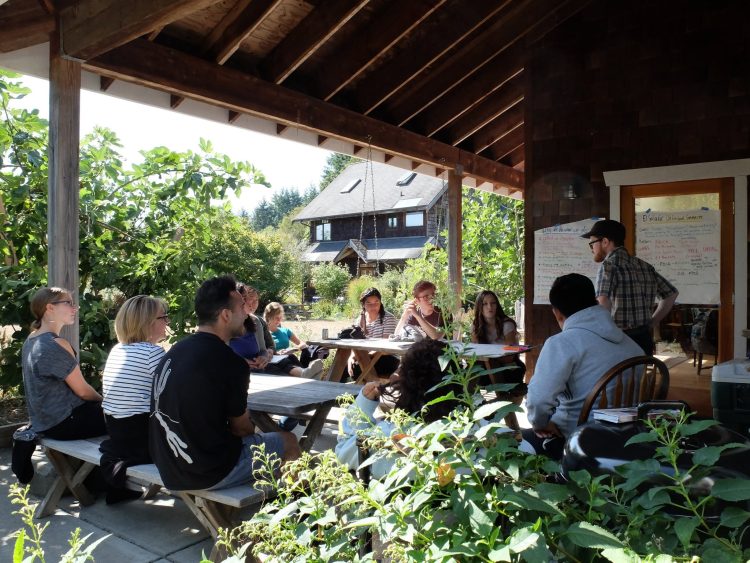 Students sit outside around picnic tables, big sheets of paper hung around with things written down.