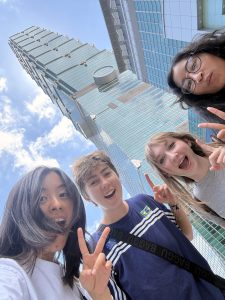 Students hold up peace sign gestures in front of skyscraper.